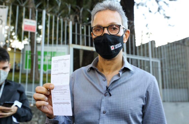 Romeu Zema de máscara exibe cartão de vacinação contra a Covid