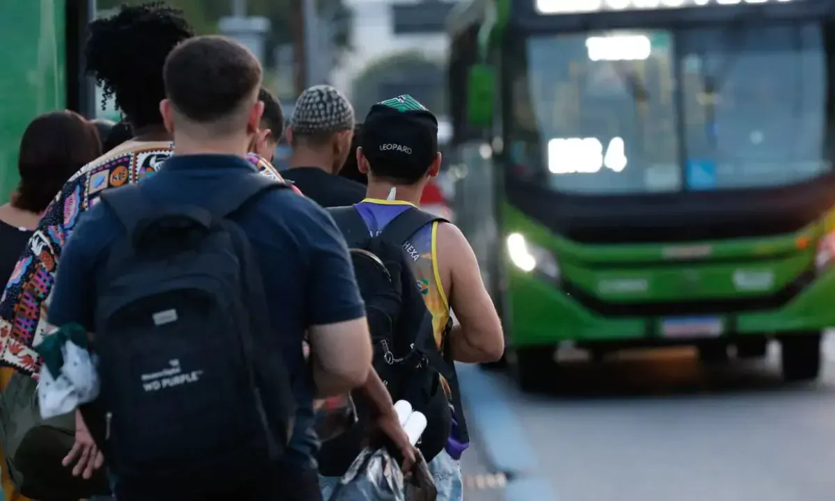 Foto mostra passageiros em fila de embarque em ônibus coletivo.