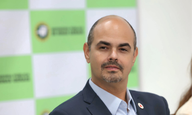 O governador Mateus Simões (PSD) em primeiro plano, com backdrop da Defensoria Pública de Minas Gerais ao fundo.