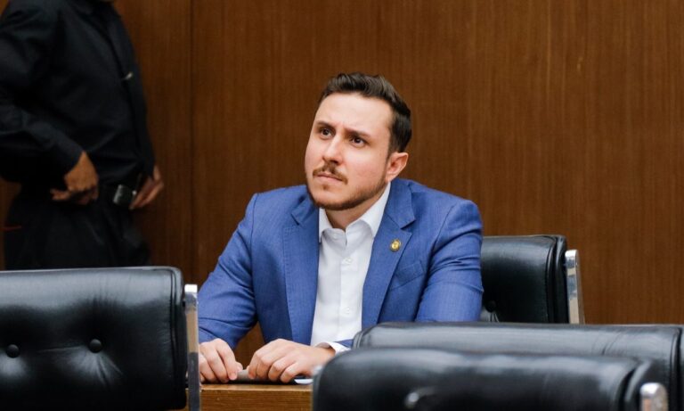 Lucas Ganem de terno azul e camisa branca, com expressão fechada, no plenário da Câmara de BH