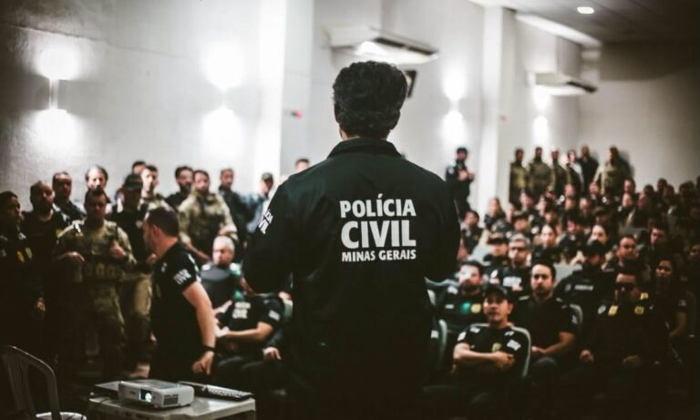 Policial civil de costas, com jaqueta da Polícia Civil de Minas Gerais, fala para um auditório cheio de agentes