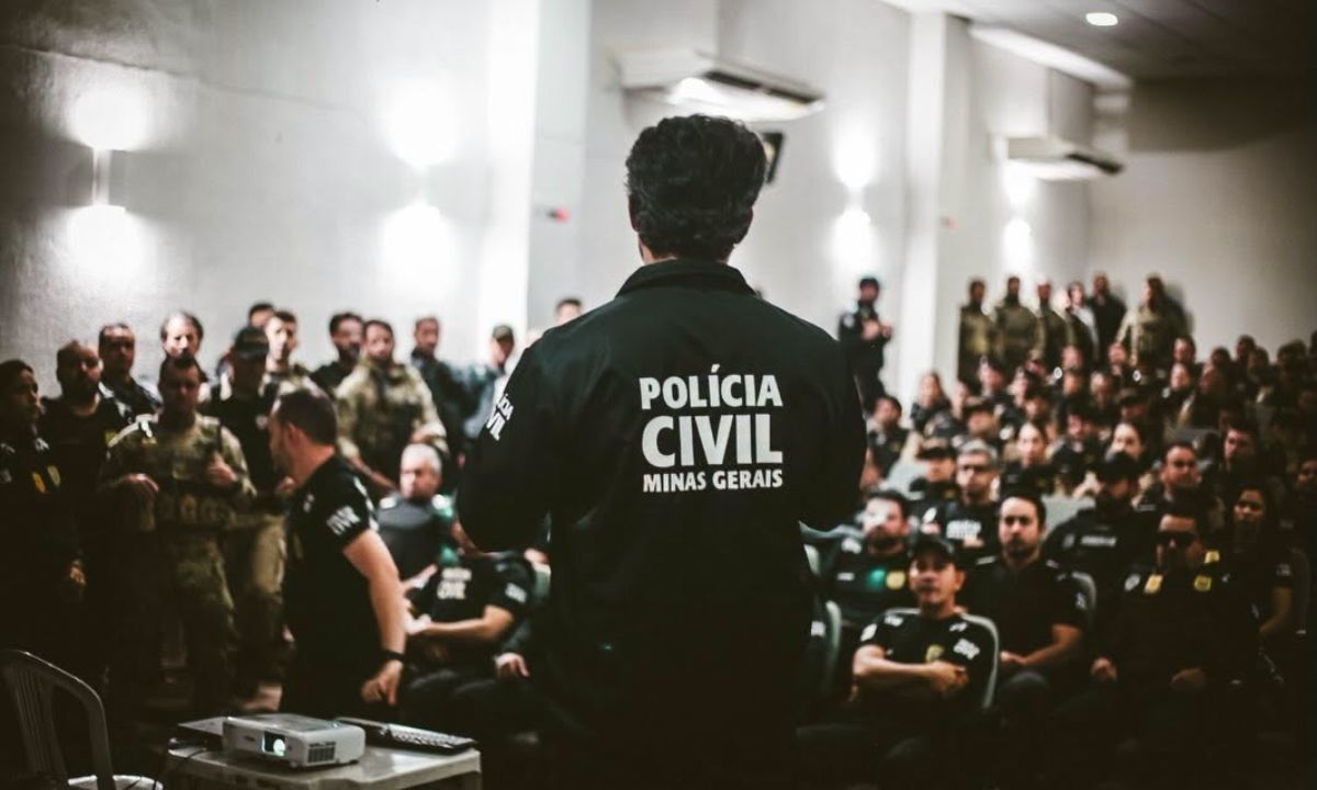 Policial civil de costas, com jaqueta da Polícia Civil de Minas Gerais, fala para um auditório cheio de agentes